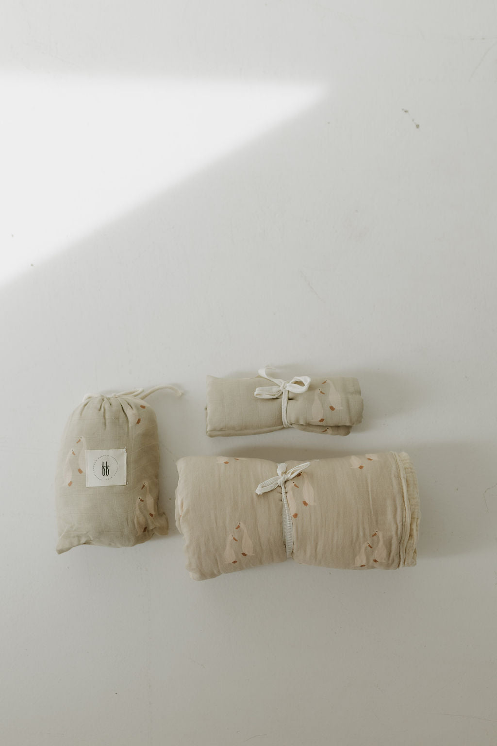 Three Muslin Quilt | Silly Goose blankets by forever french baby—one rolled, one folded, and one in a drawstring pouch—are displayed on a white surface, ideal for creating a cozy nursery with soft natural light.