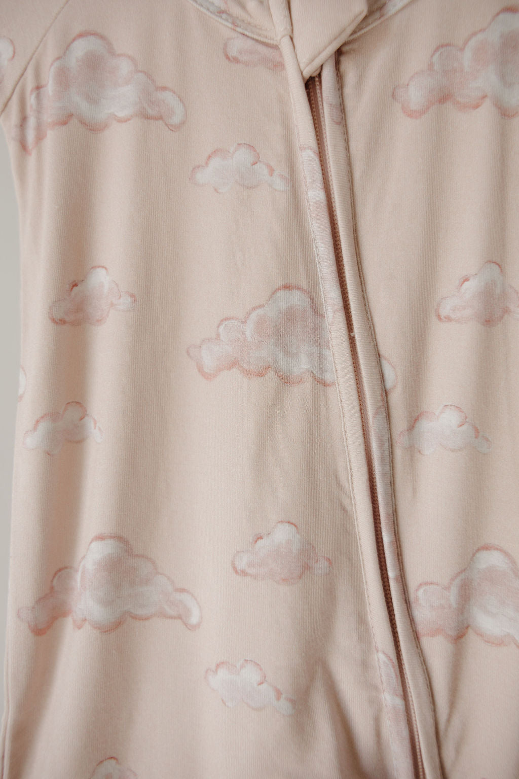 Close-up of the Kendy 3 Bamboo Zip Shortie | Ruby: a soft, pale pink fabric with light pink cloud patterns and a zip, crafted from premium hypo-allergenic bamboo for gentle comfort on little ones.