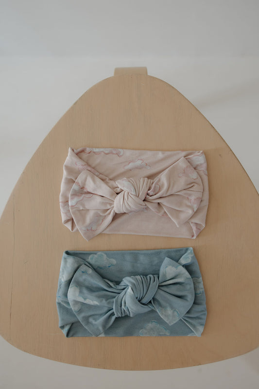 Two Bamboo Head Wraps | ff x kendy by Kendy 3, one pink and one blue with cloud patterns, are displayed on a light wooden surface. These soft bamboo headbands offer comfort and cute style for babies.