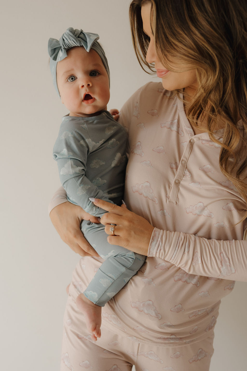 A woman in light pink cloud pajamas holds a baby wearing blue pajamas and a Kendy 3 Bamboo Head Wraps | ff x kendy, with both facing the camera against a neutral background.