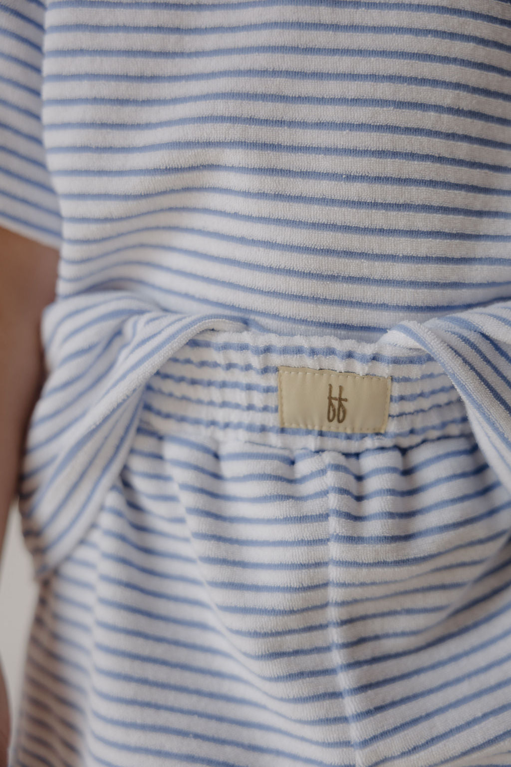 Close-up of the forever french baby Child Terry Short Set | Ocean Stripe, showing light blue and white striped fabric with an elastic waistband and a small beige "bb" tag stitched on.