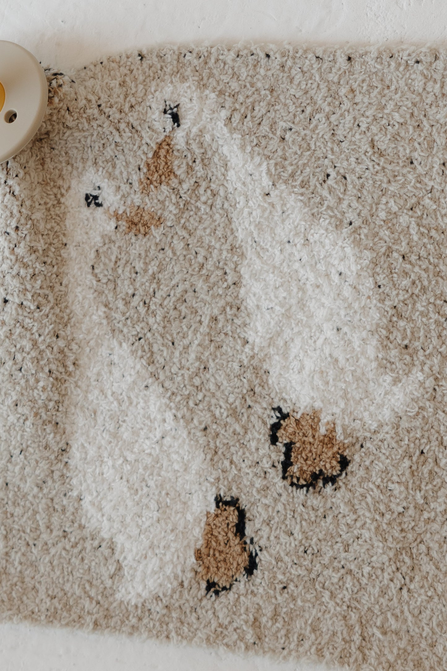A close-up of the Lovey | Silly Goose by forever french baby—a textured beige microfiber feather yarn rug with two white ducks, brown beaks and feet, plus a beige pacifier partly shown in the top left corner.