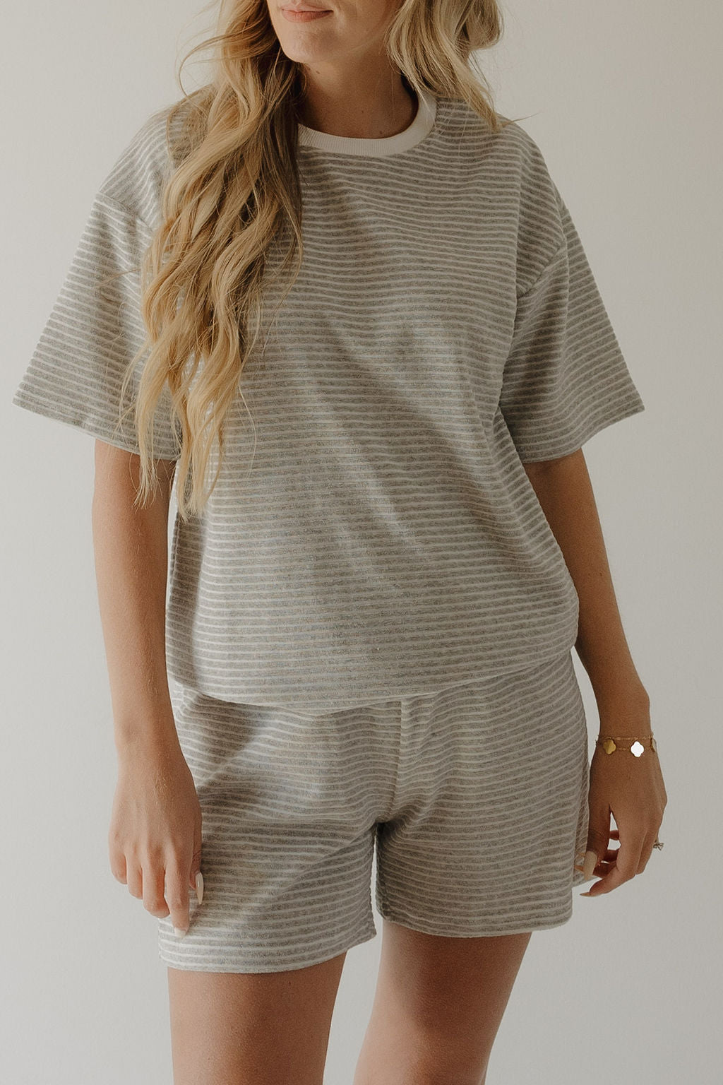 A woman with long, wavy blonde hair wears the forever french baby Women's Terry Short Set in Grey Stripe—matching shorts included—as she stands against a plain light background.