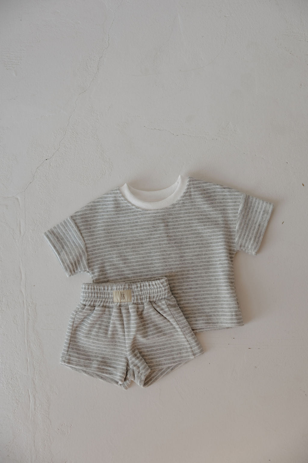 The Child Terry Short Set | Grey Stripe from forever french baby features a short-sleeved light gray and white striped shirt with elastic waist shorts—ideal for sweet family moments. Shown laid flat on a light textured surface.