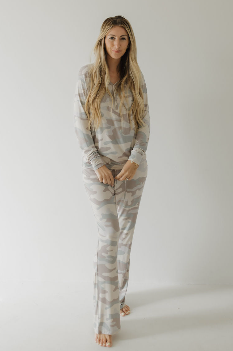A woman with long, wavy blonde hair stands barefoot against a white background, wearing forever french baby's Women's Bamboo Pajama | Camo—a light camo-print lounge set with long sleeves and drawstring pants in breathable fabric.