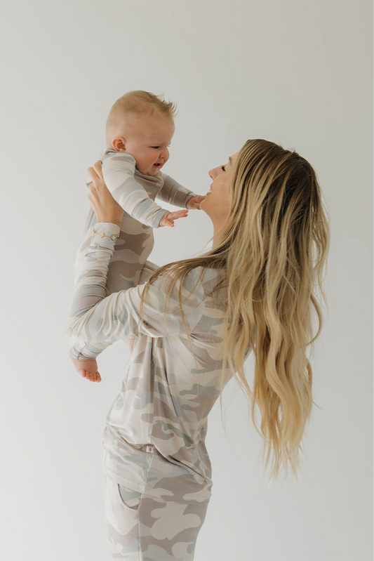 A woman with long blonde hair holds a smiling baby aloft, both dressed in matching forever french baby Women's Bamboo Pajama | Camo against a plain light background.