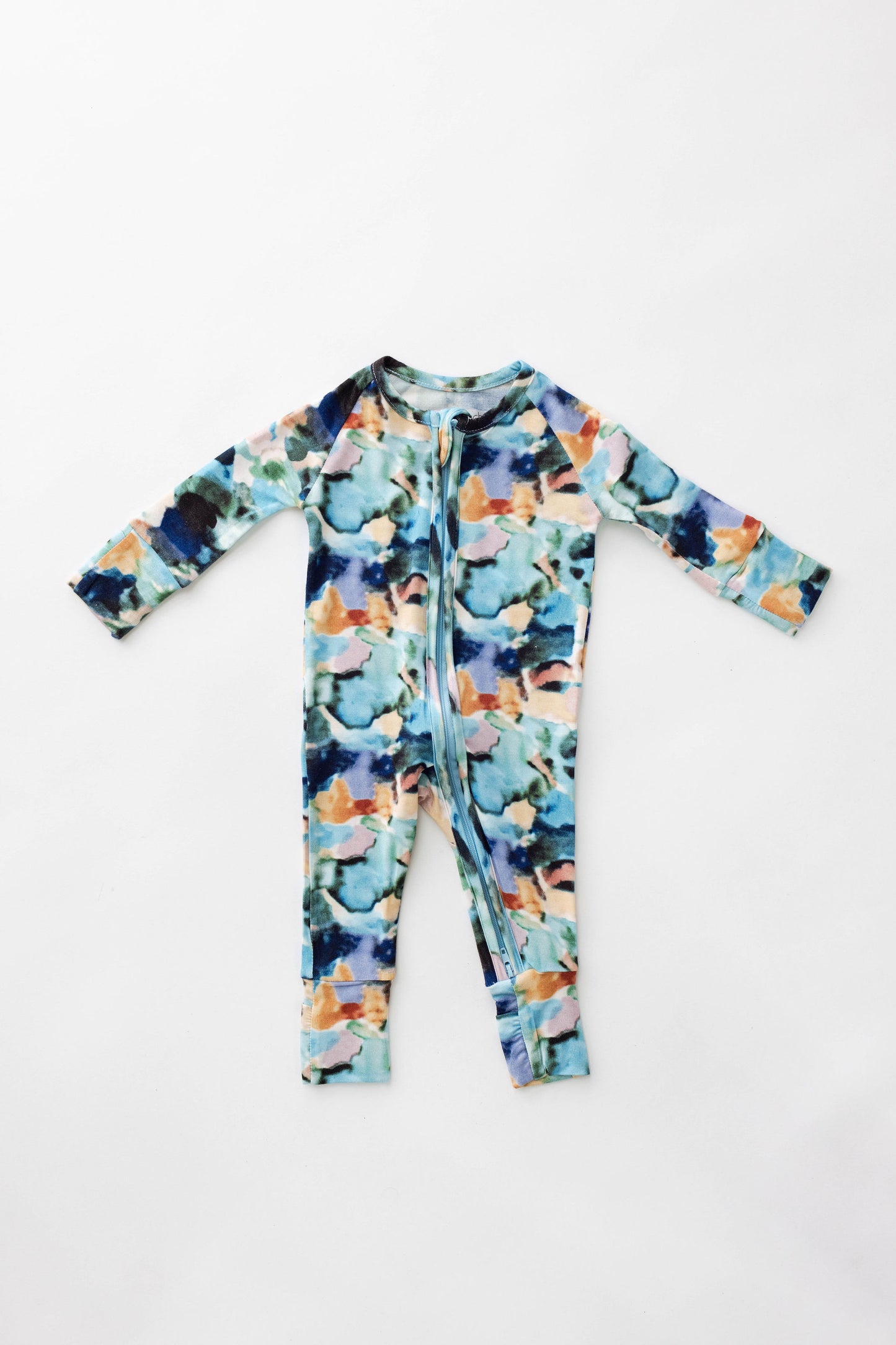 The Bamboo Zip Pajamas | Charli Print by forever french baby is a long-sleeved romper featuring a colorful abstract pattern with shades of blue, green, orange, and black. Made from soft bamboo fabric, this romper boasts a front zipper that extends from the neck to the left leg and has ribbed cuffs on both the sleeves and ankles. The garment is displayed laid flat on a white background.