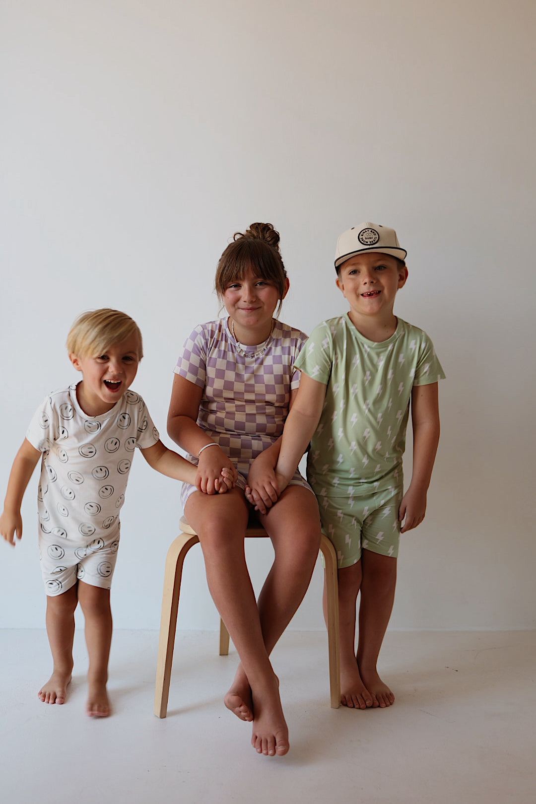 Three young children pose against a light background. Dressed in forever french baby’s Bamboo Short Set | Green Smiles, they smile and hold hands, radiating joy in hypoallergenic, breathable kids’ sleepwear.