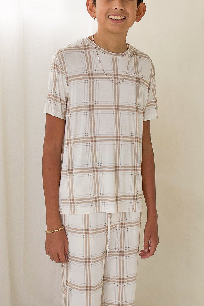A child wearing a short-sleeved, hypo-allergenic Youth Straight Leg Bamboo Pajamas | Ellis Plaid set in a tan and white plaid pattern.