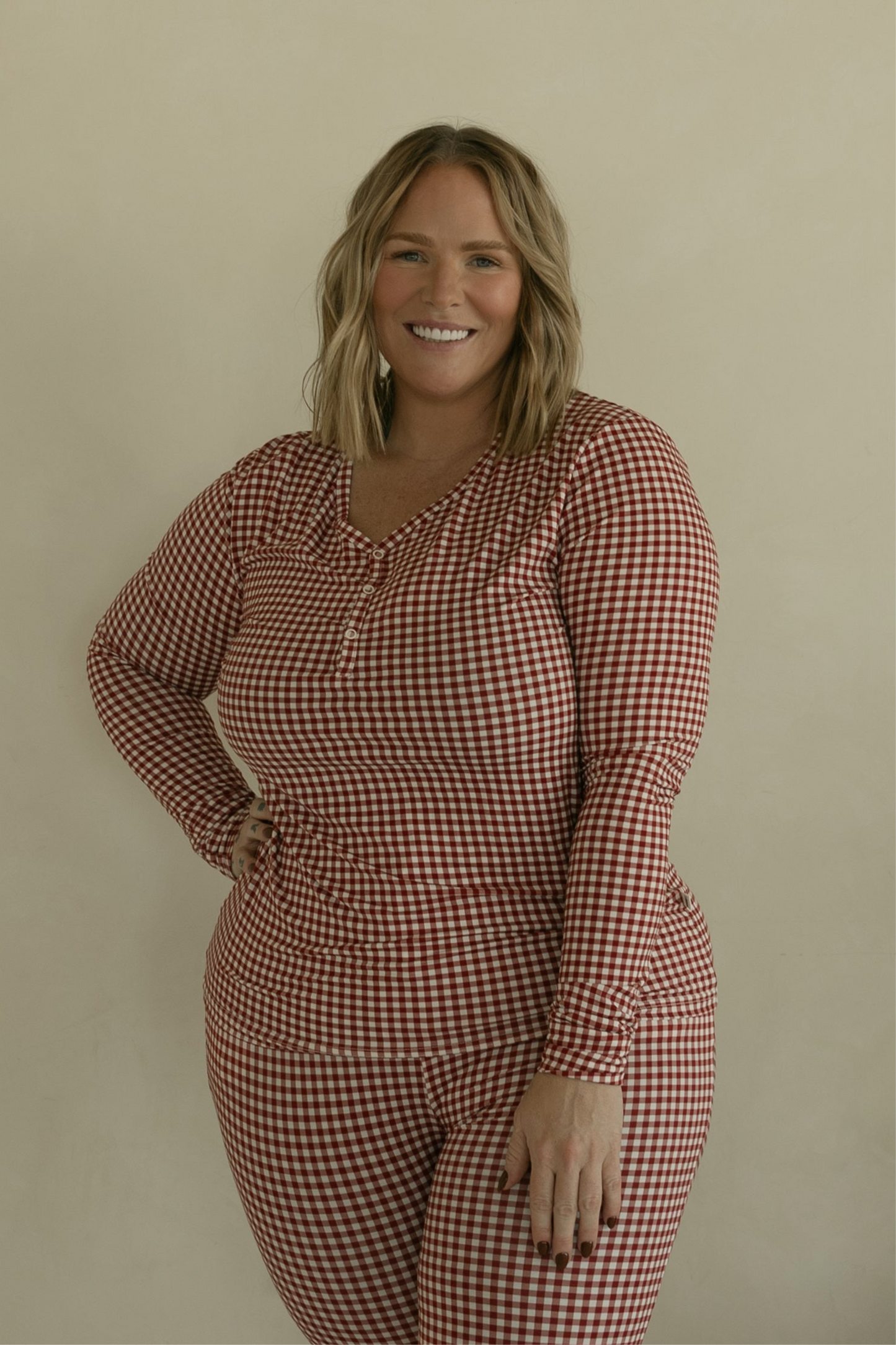 A smiling woman with blonde, shoulder-length hair wears forever french baby's Women's Bamboo Pajamas in Red Gingham, standing against a plain beige background.
