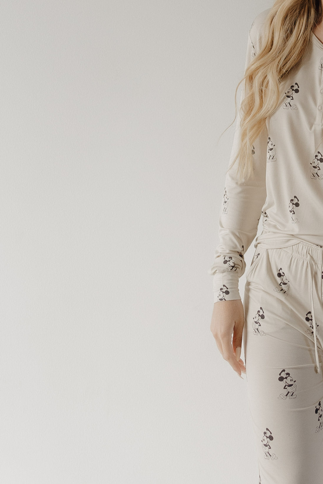 A woman in forever french baby's cream-colored Women's Bamboo Pajama | All Aboard! with a dog print stands against a plain background, only her right side visible and long wavy hair draping over one shoulder.