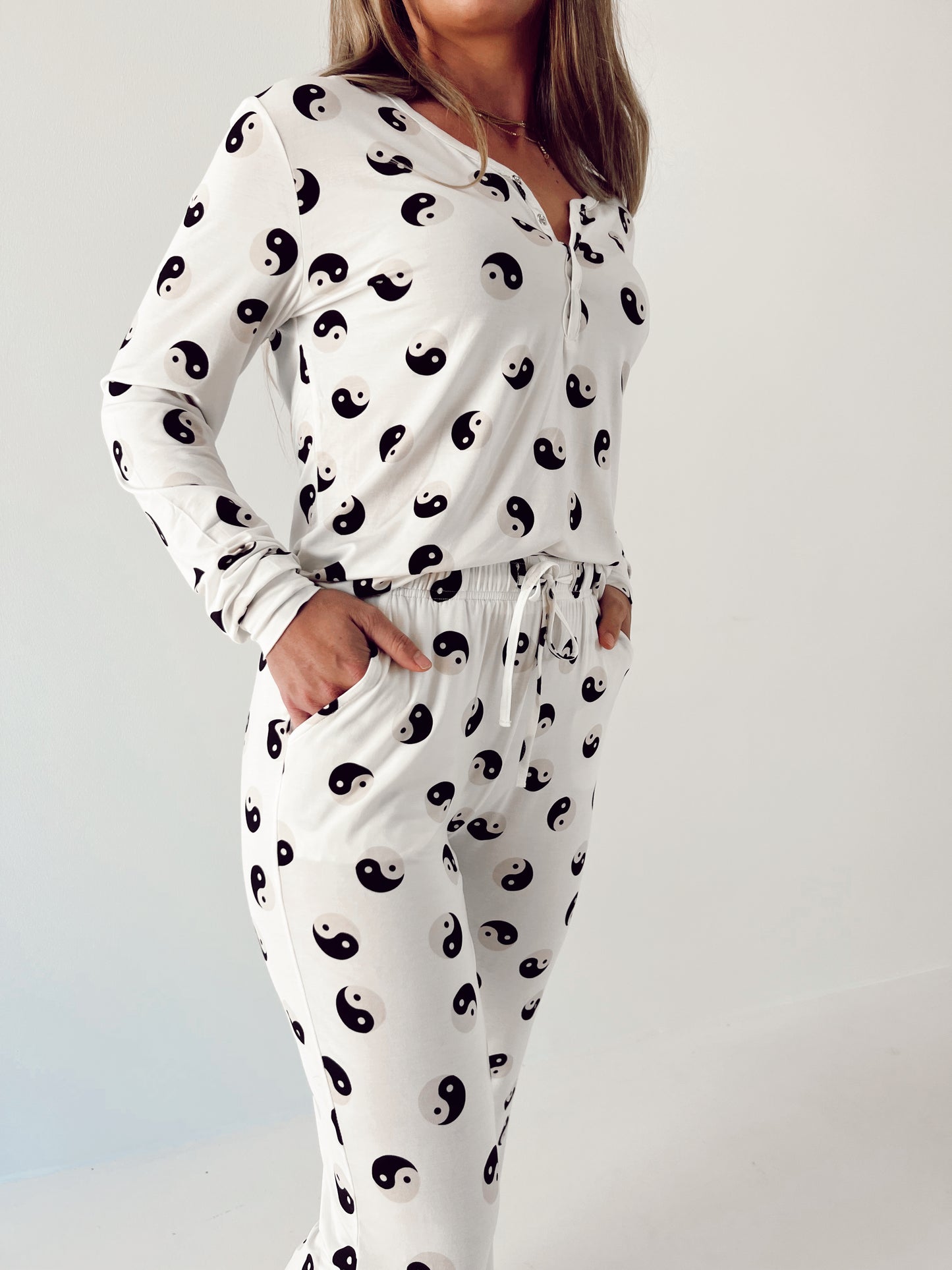 A person wearing the Women's Bamboo Pajamas in a Black & White Yin Yang pattern by forever French baby. The pajama top is breastfeeding friendly with long sleeves and buttons down the front, while the matching bottoms feature a drawstring waist. The person has their hands in the pockets of the pants.