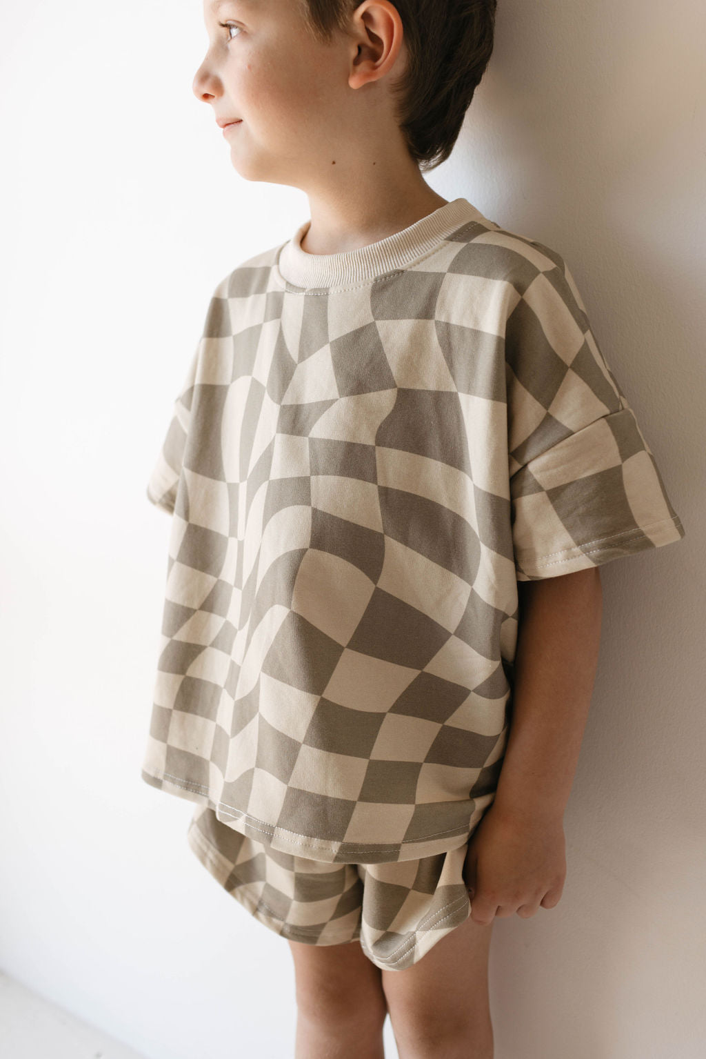 A young child stands in profile against a white background, wearing the Short Set | Wavy Checkerboard from forever french baby. This trendy children's clothing piece is both stylish and comfortable.