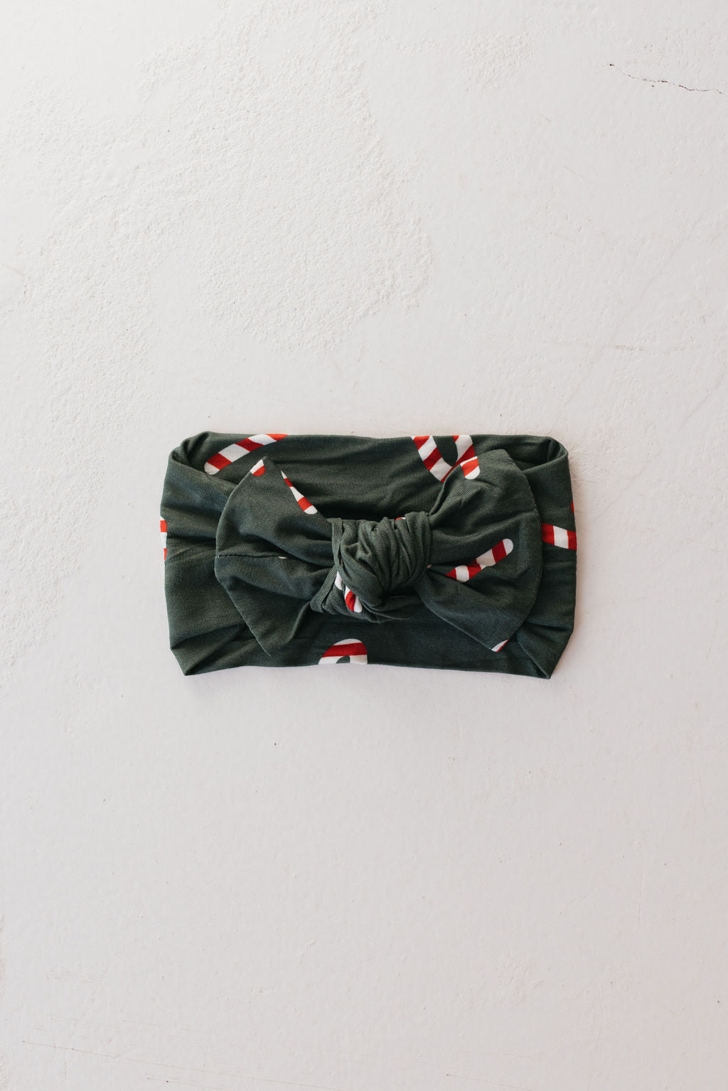 The Bamboo Head Wrap | Candy Cane Lane by forever french baby is made from soft bamboo material and showcases a green fabric adorned with candy cane patterns, complete with a central knot, elegantly styled on a light gray surface.