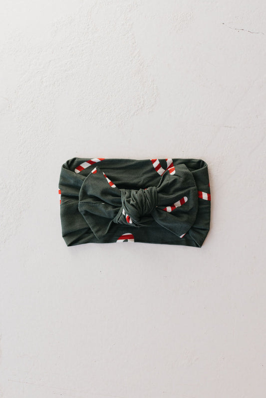 The Bamboo Head Wrap | Candy Cane Lane by forever french baby is made from soft bamboo material and showcases a green fabric adorned with candy cane patterns, complete with a central knot, elegantly styled on a light gray surface.