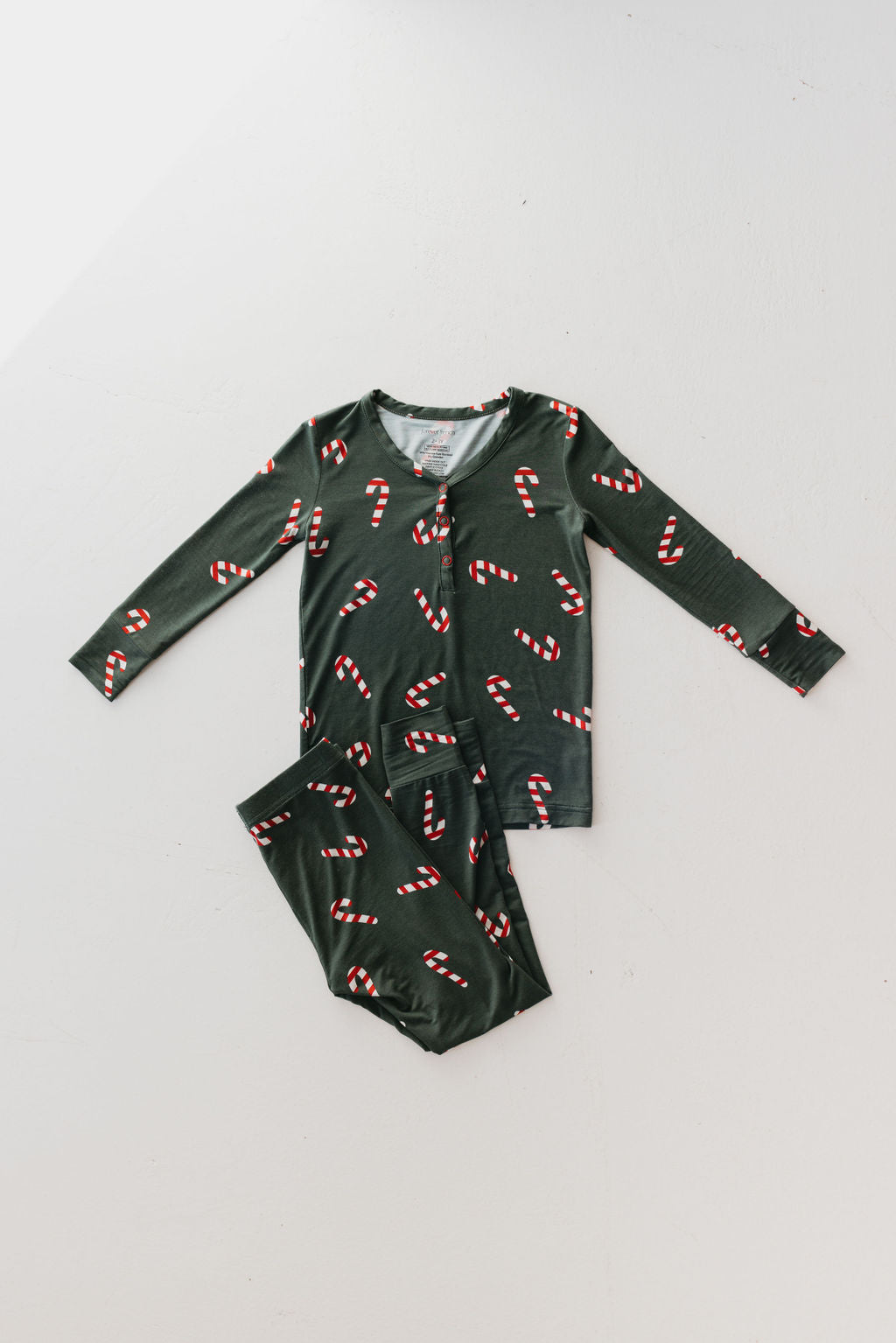 The "Candy Cane Lane" bamboo two-piece pajamas from forever french baby are laid flat on a white surface. This breathable sleepwear set features a long-sleeve button-up top paired with matching pants, promising comfort for a restful night’s sleep.