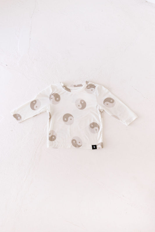 The forever french baby Long Sleeve Bamboo T-Shirt features a beige and white yin-yang design on breathable fabric, displayed flat on a white textured background.