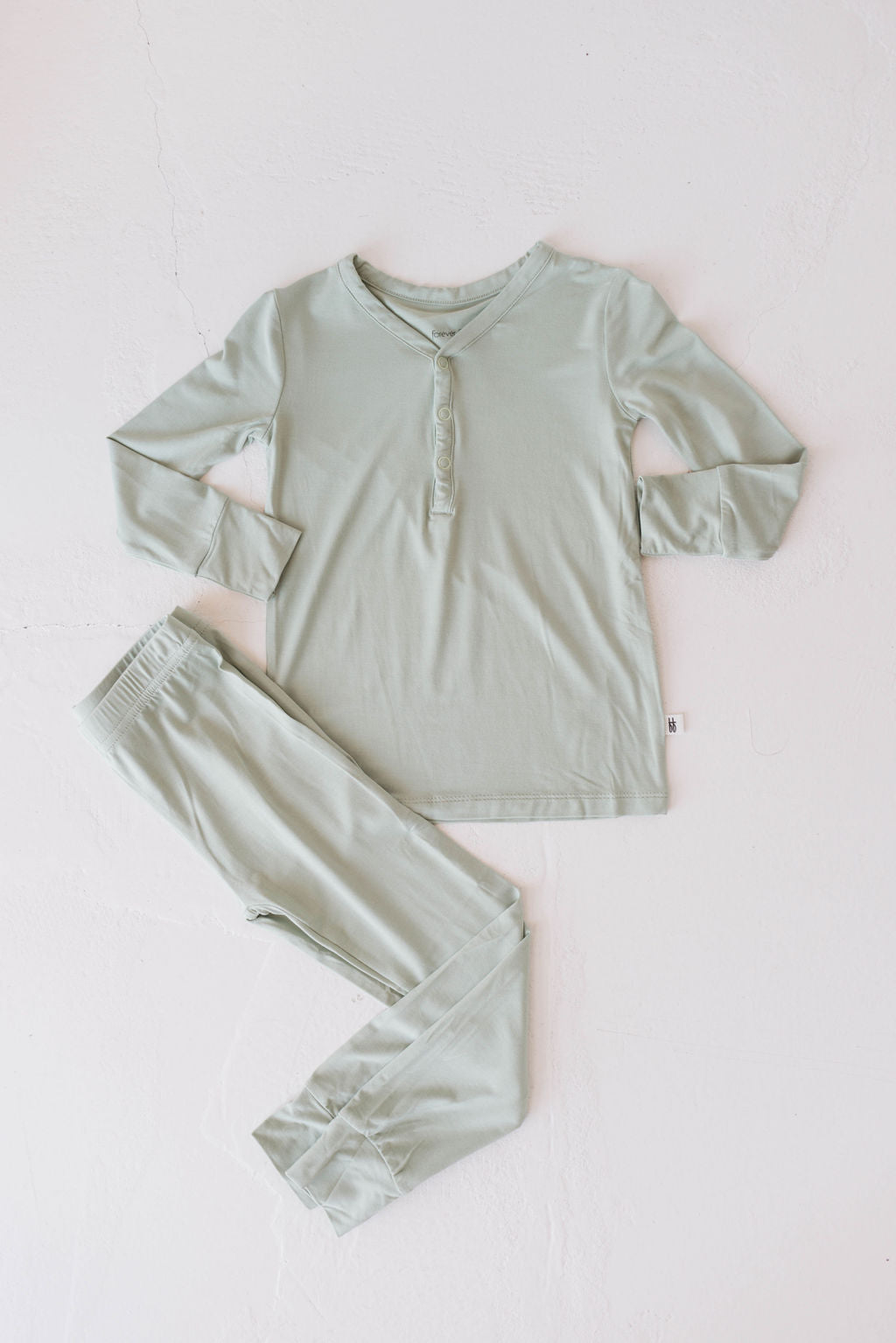 The "Bamboo Two Piece Pajamas | Pistachio" by forever french baby, featuring a light green color, breathable bamboo fabric, a long-sleeve top with buttons at the neckline, and matching pants with an elastic waistband, is neatly laid out on a white background.