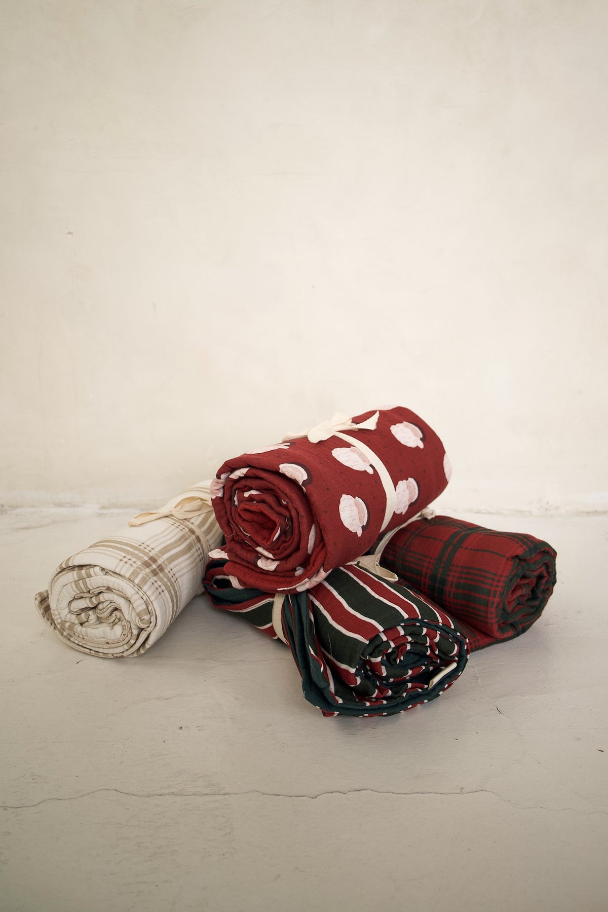 Four rolled Muslin Quilt | Christmas Plaid baby quilts in patterns including red Christmas plaid, green and red stripes, white dots on red, and beige plaid.