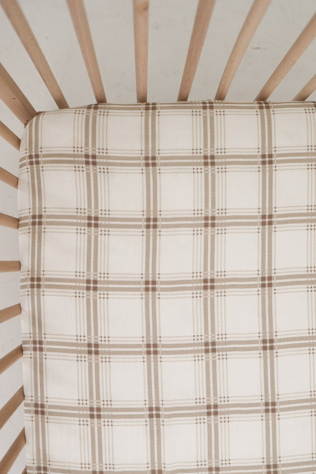A top view of a crib with light wooden slats and a mattress covered in the forever french baby Muslin Crib Sheet | Ellis Plaid, perfect for adding cozy style to your baby nursery bedding.