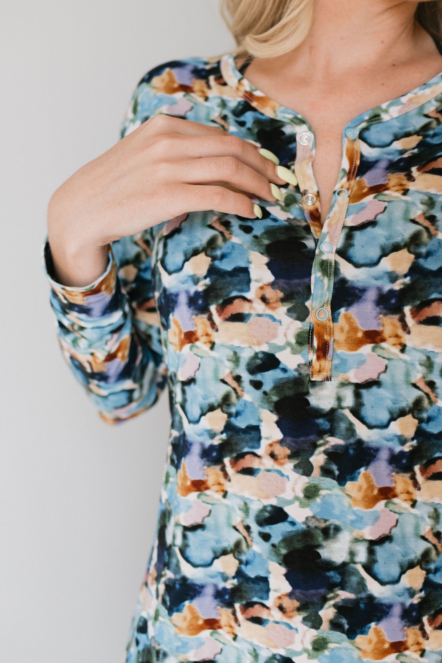 A person is shown from the shoulders down, wearing the Women's Bamboo Pajamas in Charli Print by forever french baby. The long-sleeved shirt features a vibrant, abstract, multicolored pattern with a partial button-down front and three buttons. The person's right hand is touching the collar area near the buttons, capturing the essence of Charli French's bold artistic style.