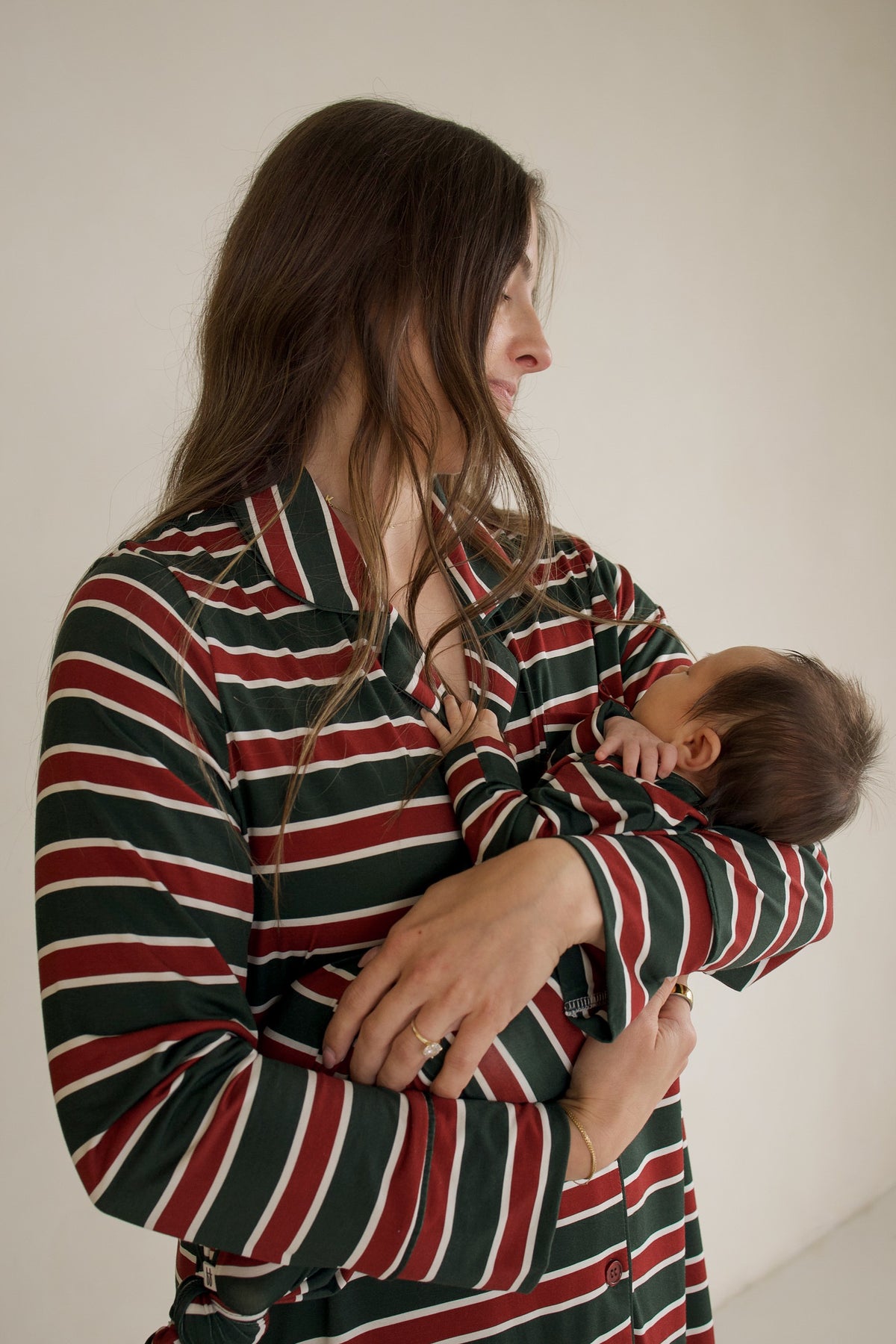 A person wearing a long-sleeved shirt with red, green, and white stripes holds a baby wearing a matching Bamboo Knotted Gown | Holiday Stripe.