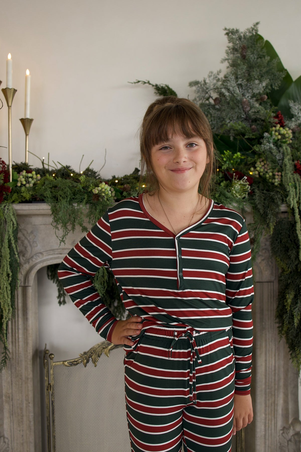 A girl wears forever french baby Youth Flare Bamboo Pajamas | Holiday Stripe, featuring a long-sleeved shirt and pants with red, green, and white stripes in hypoallergenic bamboo fabric.