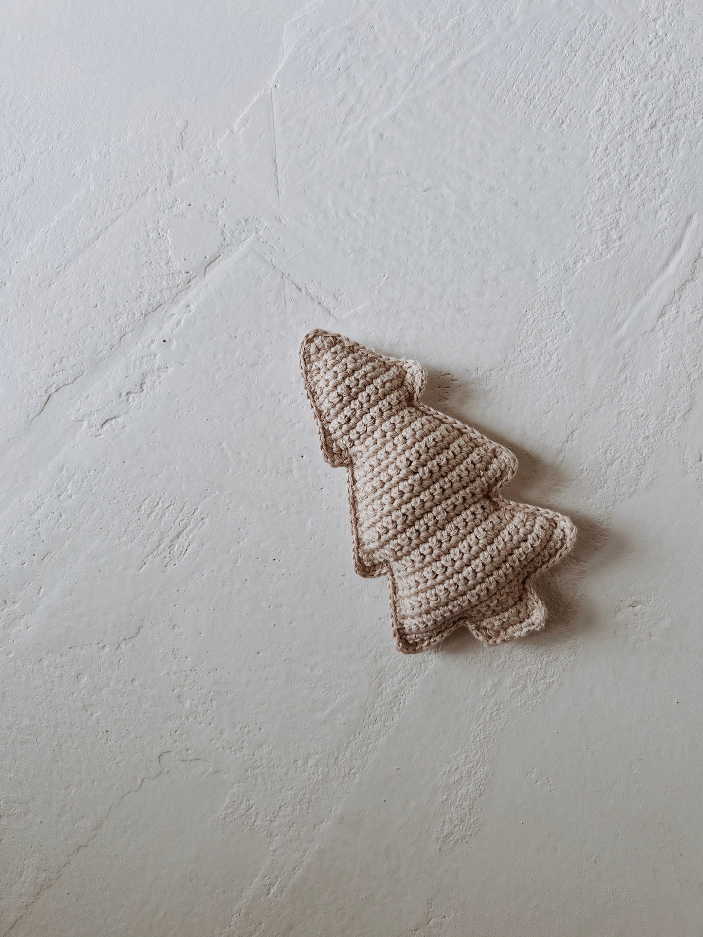A charming and timeless touch for a baby Christmas atmosphere is created by the Beige Knit Tree Rattle from Forever French Baby, as it sits on a textured white surface.