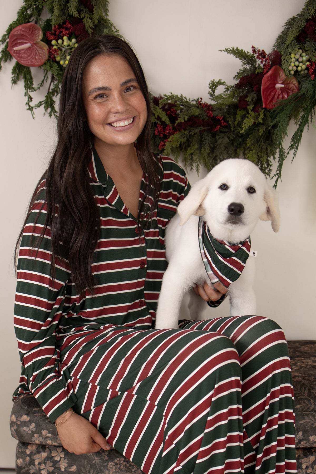 A smiling woman wearing matching bamboo viscose holiday-striped pajamas holds a white puppy wearing a Bamboo Bandana | Holiday Stripe.