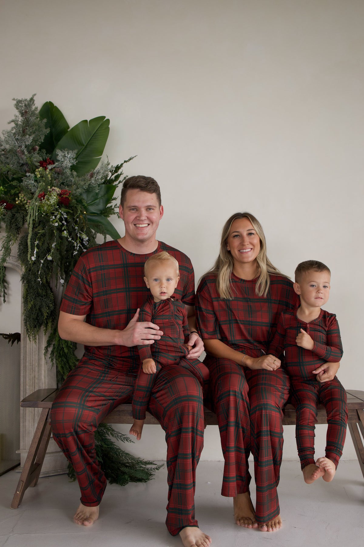 A family of four wearing matching Bamboo Two Piece Pajamas | Christmas Plaid sitting together on a bench.