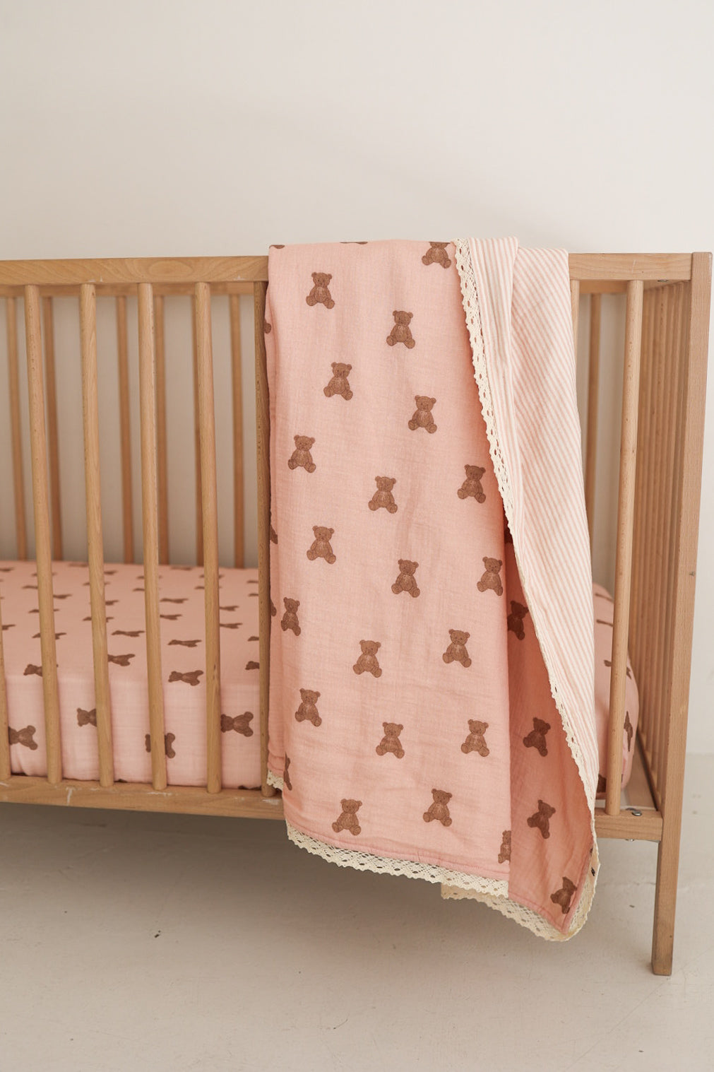 A wooden crib with the forever french baby Muslin Crib Sheet | Pink Lottie and a matching teddy bear blanket draped over the side creates a cozy, charming nursery look.