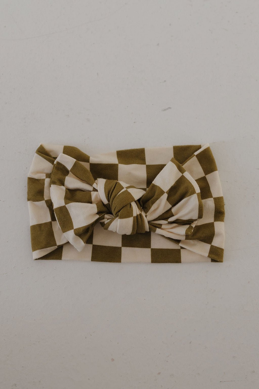 The forever french baby Bamboo Head Wrap in Olive Checkerboard features a large center knot and an olive green and white check pattern, shown laid flat on a light surface.