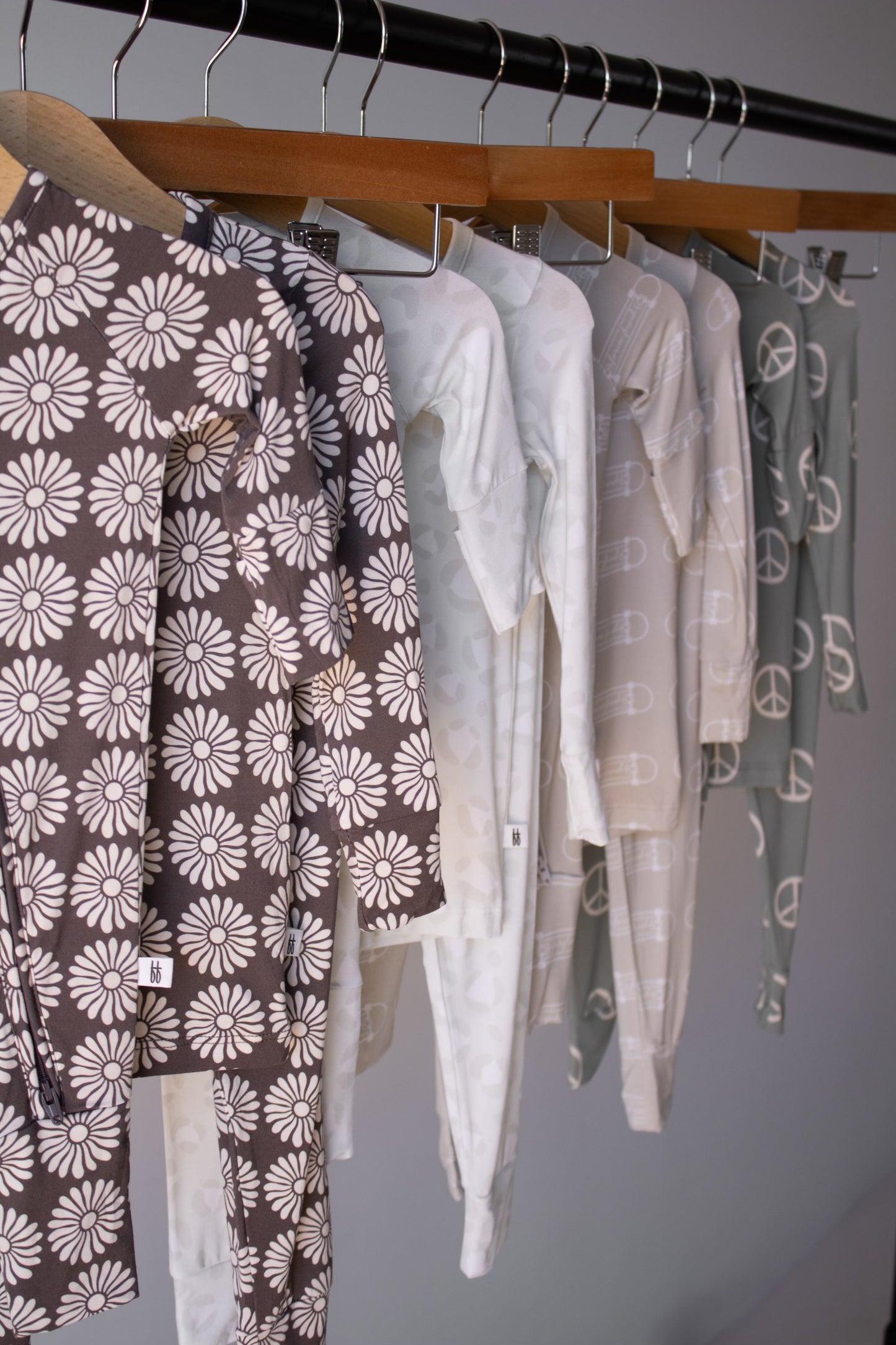 Bamboo Two Piece Pajamas | Retro Floral by forever french baby—hypoallergenic kids’ clothing in soft neutral tones, featuring daisies, hearts, peace signs, and geometric shapes—hang neatly on wooden hangers for stylish comfort.