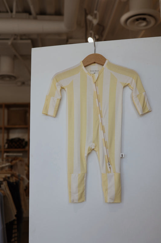 The Bamboo Zip Pajamas | Butter by forever french baby, featuring yellow and white stripes, long sleeves, and a front zipper in breathable sleepwear fabric, hangs on a wooden hanger against a white wall in the store.