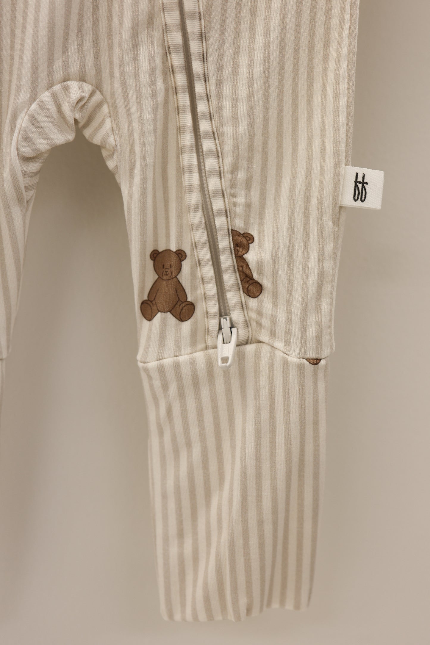 The forever french baby Bamboo Zip Pajamas | Teddy feature cream and beige stripes, a footed one-piece zip design, two small brown teddy bear accents on the leg, and a white "bf" tag on the side seam.