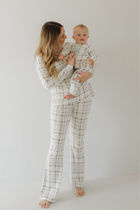 A woman holds a baby, both barefoot against a white background, wearing matching forever french baby Women's Bamboo Pajamas in Picnic Plaid.