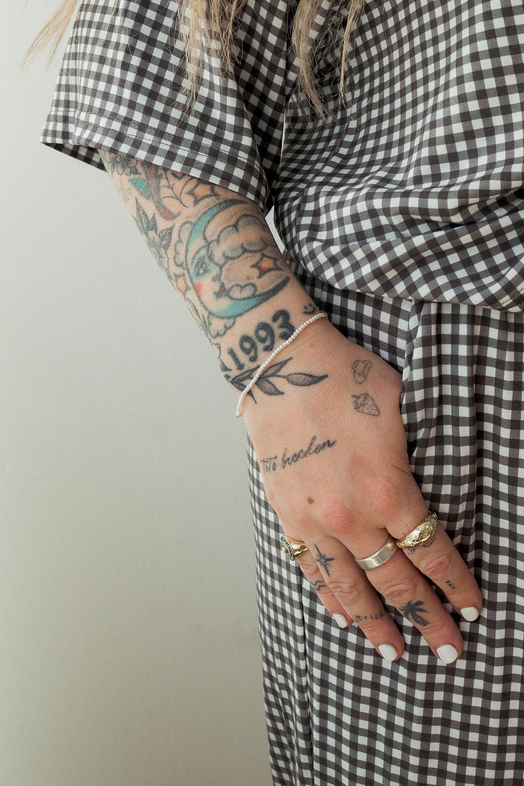 A tattooed hand with silver rings and white nails rests on the hip, modeling the forever french baby Women's Boxy Tee Lounge Set in Green Gingham—showcasing a casual, cool, and hypo-allergenic style.