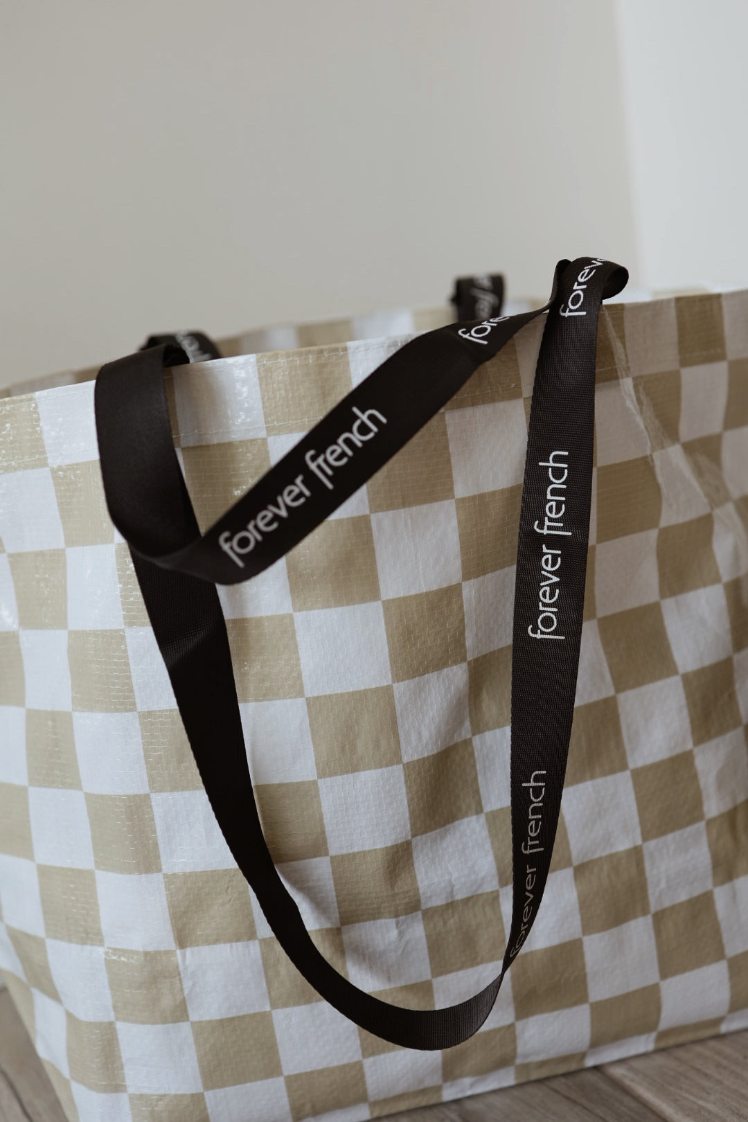 The ff Warehouse Sale Tote by forever french baby features a large beige and white checkered design with black handles displaying "forever french" in white text, shown on a wooden floor against a light wall.