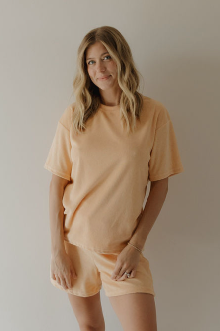 A woman with wavy blonde hair wears the forever french baby Women's Terry Short Set in Sherbert, standing against a plain background and smiling slightly.