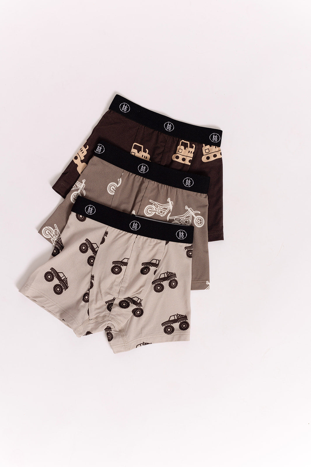 The forever french baby Bamboo Boxers (3 Pack) feature dirt bike, bulldozer, and monster truck prints in brown, tan, and beige with black waistbands—hypoallergenic bamboo underwear designed for kids.