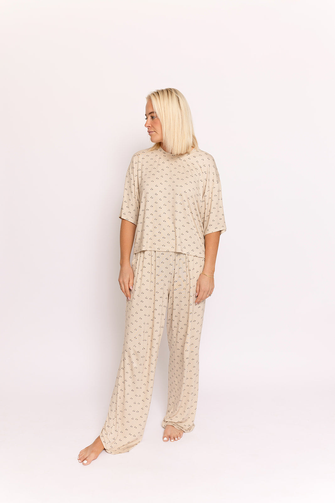 A blonde woman stands barefoot in a relaxed pose, wearing the forever french baby Women's Boxy Tee Lounge Set in Flora, featuring a loose fit and subtle pattern, against a plain light background.