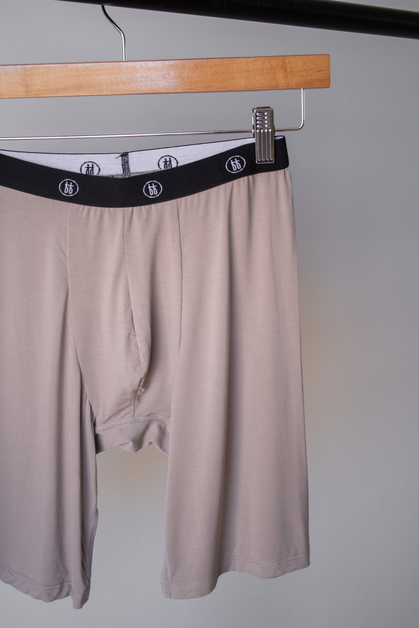A set of forever french baby Men's Bamboo Boxers (3 Pack) in checkerboard and faded brown checkerboard, crafted from soft, hypo-allergenic bamboo with a black logo waistband, shown on a wooden hanger against a light gray backdrop.