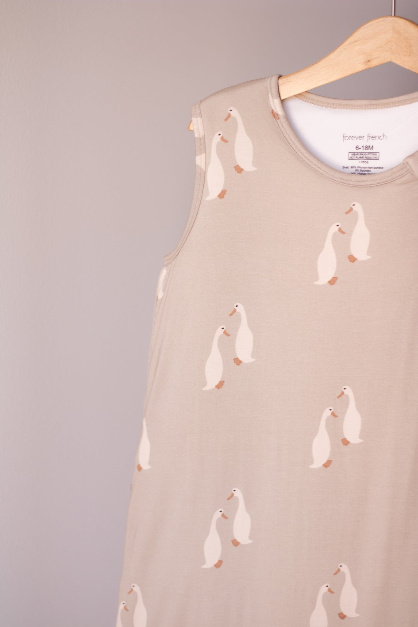 The Bamboo Sleep Sack | Silly Goose by forever french baby features a beige bamboo fabric with white geese, shown hanging on a wooden hanger against a light gray background. This cozy wearable blanket keeps your baby comfortable all night.