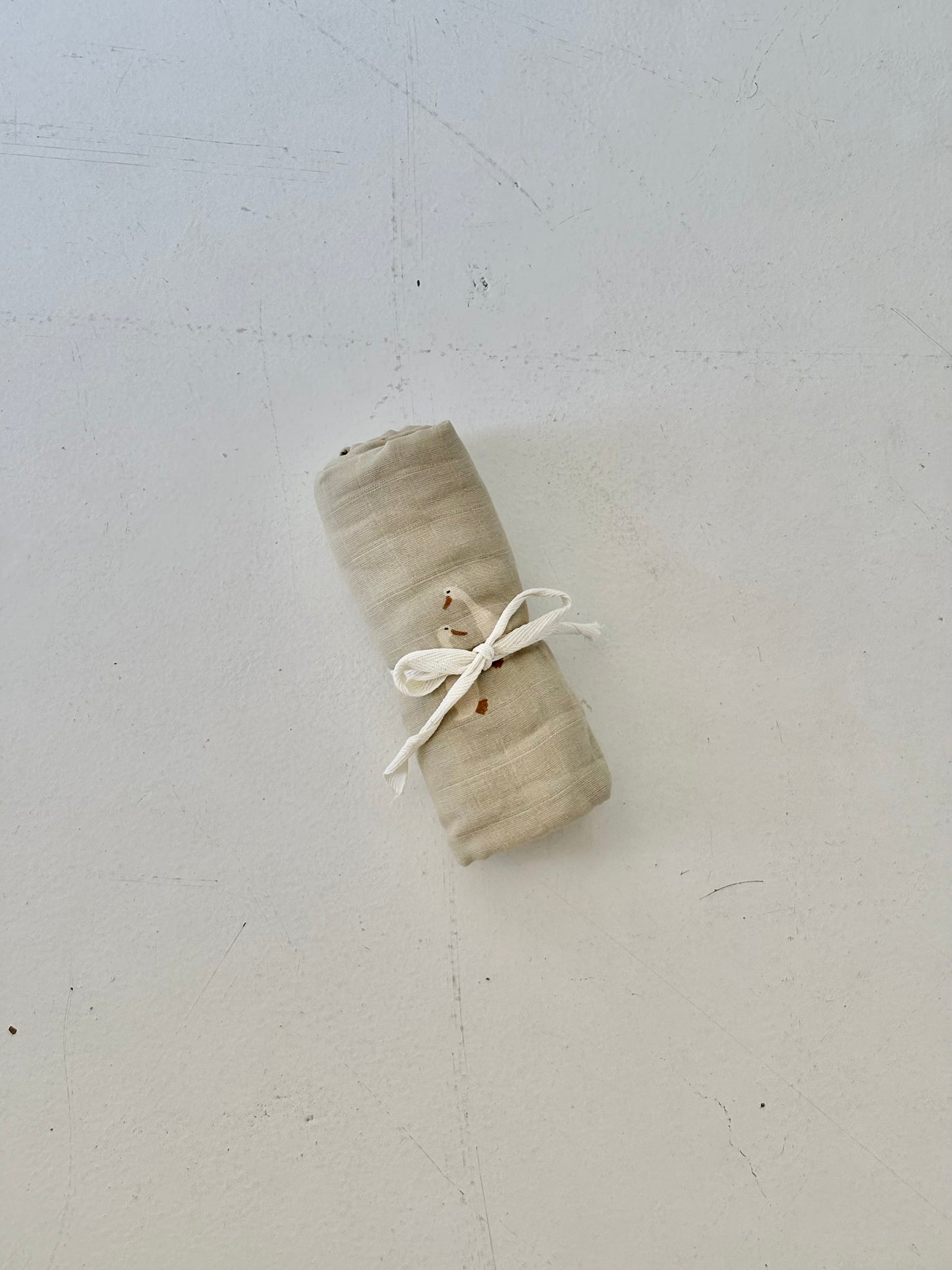 A Muslin Swaddle by forever french baby, from the Silly Goose collection, is neatly rolled and tied with a white string, resting on a lightly textured white surface.
