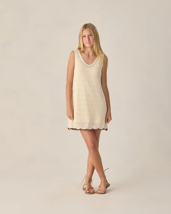 A woman stands against a plain background wearing the Rylee + Cru Crochet Tank Mini Dress in Natural, a sleeveless A-line mini dress with a V-neckline, paired with tan sandals, her arms relaxed by her sides.