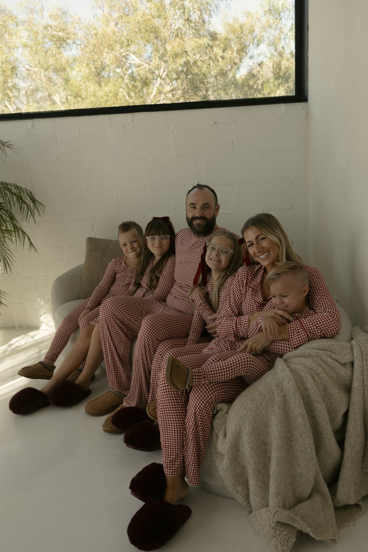 A family of six beams in a modern room, all wearing forever french baby’s Long Sleeve Women's Bamboo Pajamas in Red Gingham—hypo-allergenic, ultra-soft, and perfect for cozy moments together.
