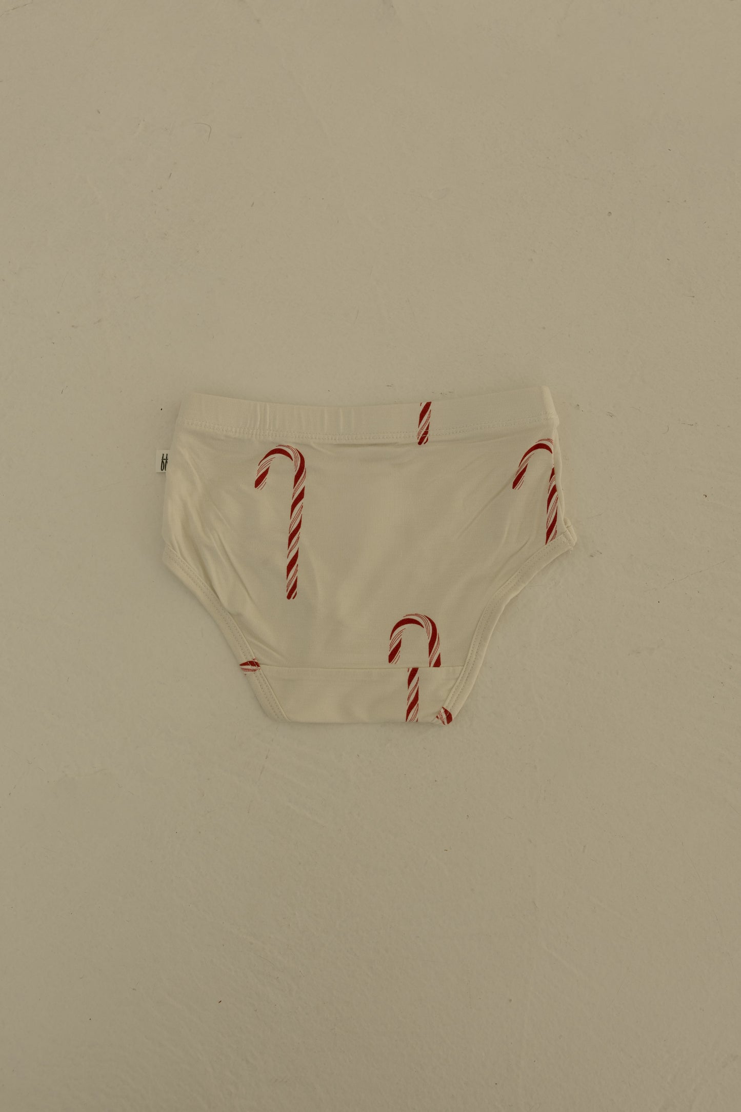 A pair of forever french baby Girl's Bamboo Briefs (3 Pack)—featuring a red candy cane print—lays flat on a light beige surface.