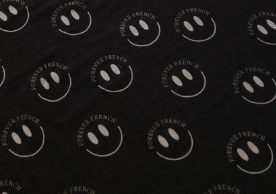 A charcoal and white muslin swaddle by Forever French Baby features a uniform grid of white smiley faces, each encircled by the words "FOREVER FRENCH BABY.