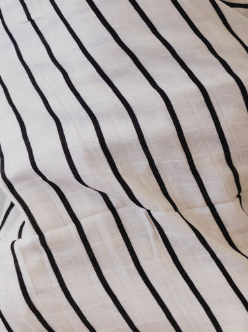 Close-up of a forever french baby Muslin Swaddle | Grey & Black Stripe, featuring a pattern of evenly spaced vertical black stripes. The fabric shows slight folds and has a textured surface.
