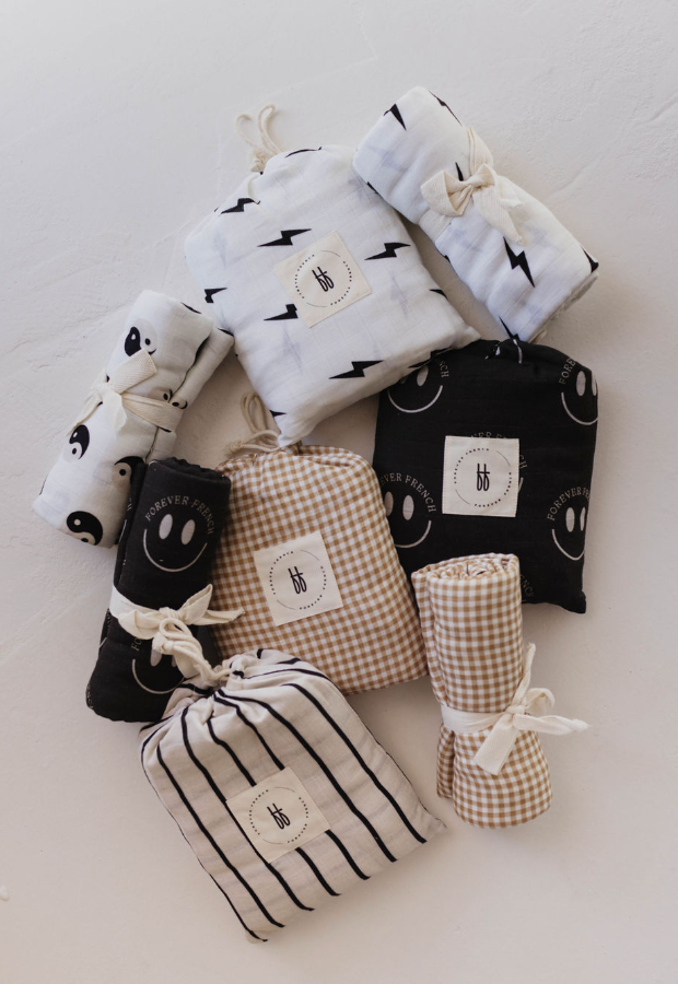 Discover a charming assortment of meticulously organized organic cotton swaddles and baby blankets from forever french baby, showcasing a variety of patterns including checkered, striped, smiley faces on black, lightning bolts on white, and the standout Muslin Swaddle | Black & White Yin Yang. Crafted from soft muslin fabric, each blanket is beautifully rolled or folded and secured with white string for a contemporary nursery touch.